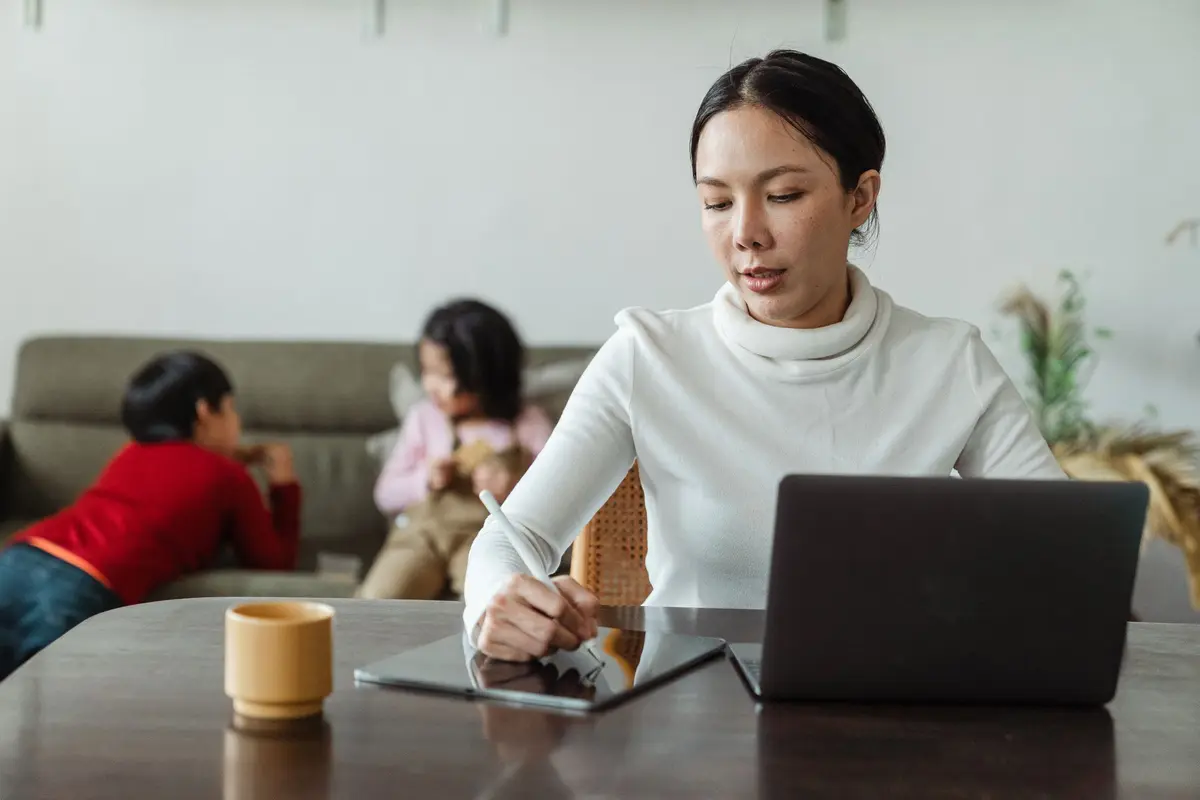 Eine Mutter arbeitet am Laptop, ihre Kinder spielen im Hintergrund