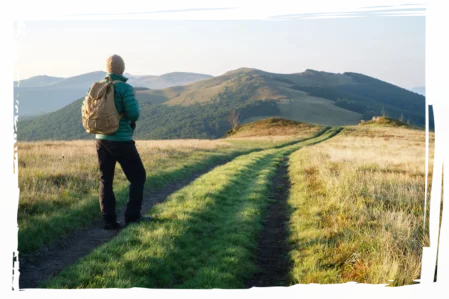 Auf dem Weg zur beruflichen Neuorientierung Mann mit Rucksack blickt in die Ferne auf einem Weg durch die Natur – Symbol für persönliche und berufliche Veränderung